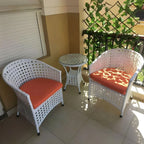 Outdoor patio set with 2 perforated armchairs and a round side table, orange cushions, white frame