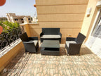 Outdoor lounge set: dark woven armchairs, loveseat, and glass coffee table with cushions
