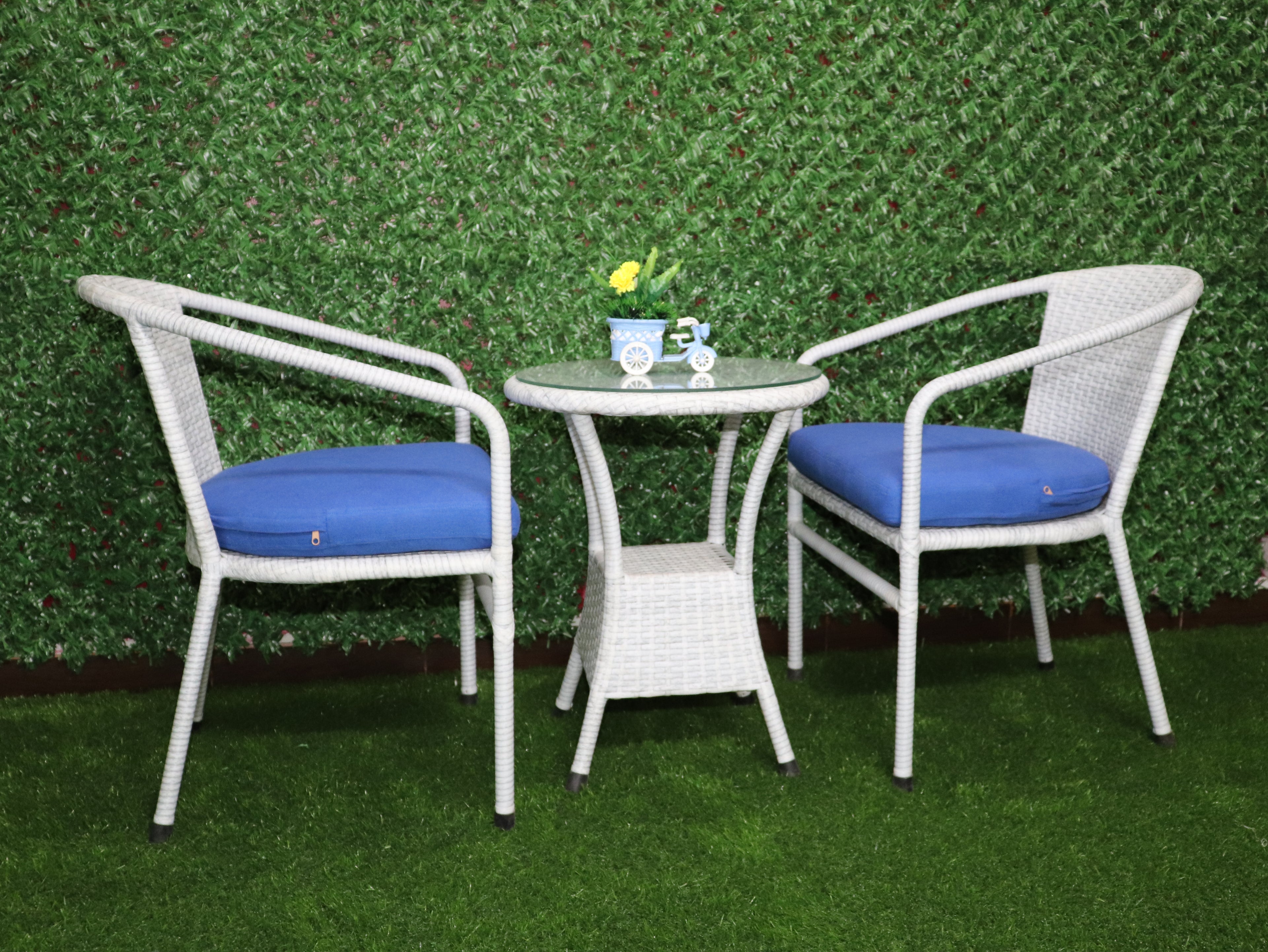 White outdoor bistro set with two chairs, blue cushions, and round glass-top table