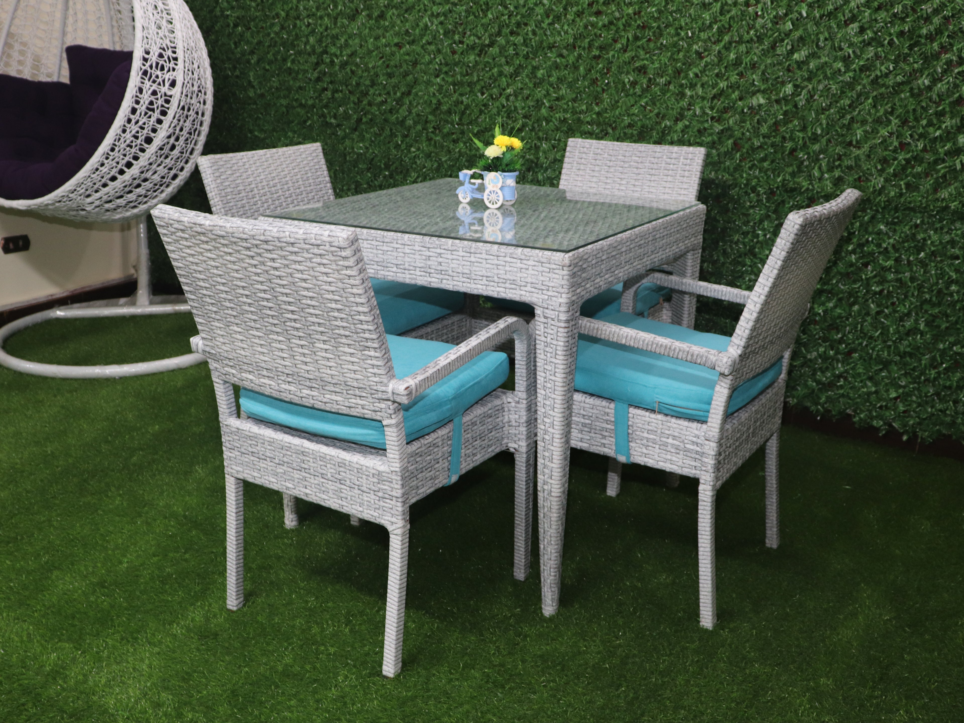 Outdoor rattan dining set for four with gray chairs and turquoise cushions around glass table
